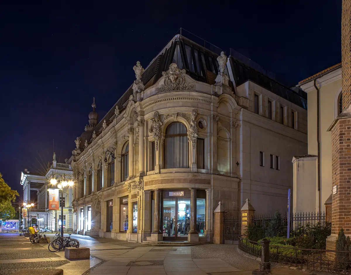 Bogato zdobiona, oświetlona nocą fasada hotelu Monopol z łukowym oknem nad narożnym wejściem